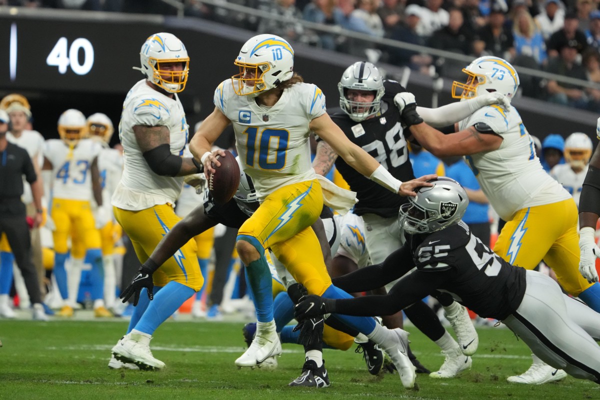 Dec 4, 2022; Paradise, Nevada, USA; Los Angeles Chargers quarterback Justin Herbert (10) carries the ball against Las Vegas Raiders defensive end Chandler Jones (55) and defensive tackle Kyle Peko (93) in the first half at Allegiant Stadium. Mandatory Credit: Kirby Lee-USA TODAY Sports