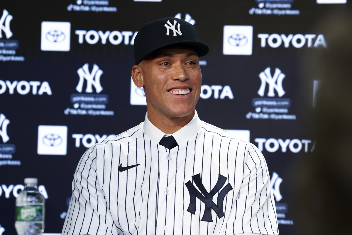 Aaron Judge smiles at a press conference in a Yankees uniform and hat