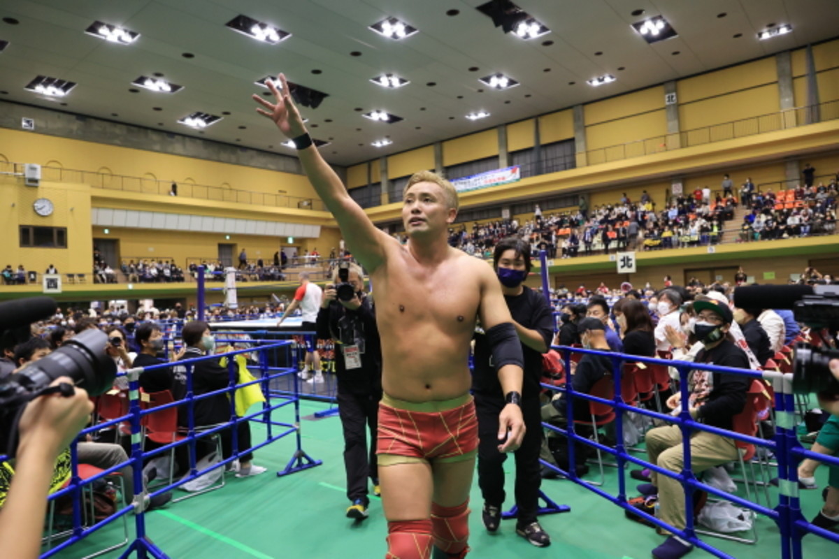a wrestler stands in the ring with a hand in the air