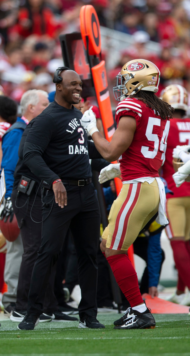 DeMeco Ryans smiles as he and Fred Warner talk on the sideline during a game