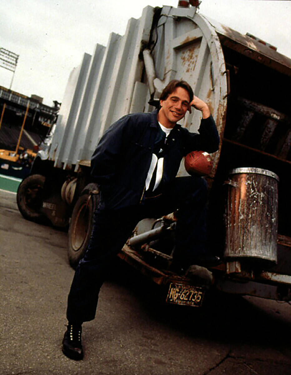 Tony Danza leans against a garbage truck with a football in a promotional shot for The Garbage Picking Field Goal Kicking Philadelphia Phenomenon