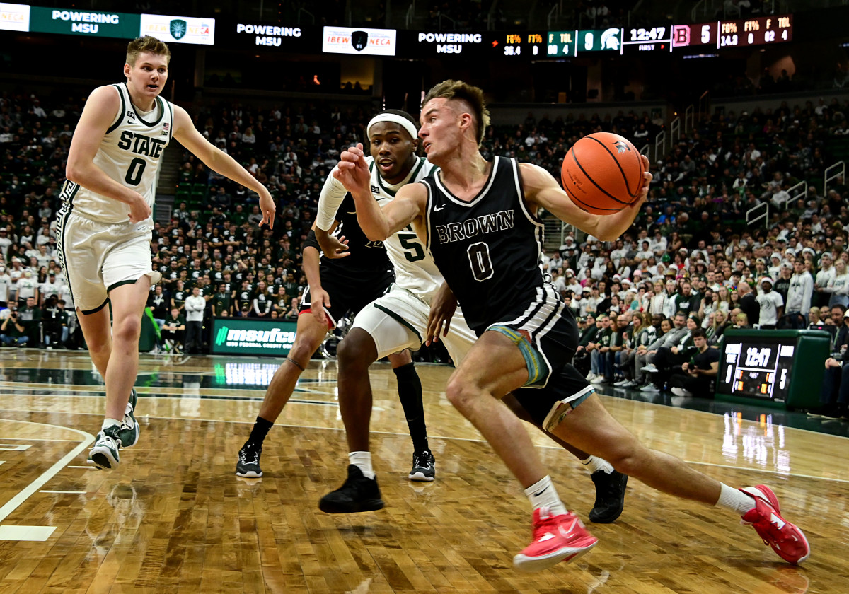 Dec 10, 2022; East Lansing, Michigan, USA; Brown Bears guard Paxson Wojcik (0) drives the baseline against Michigan State Spartans guard Tre Holloman (5) at Jack Breslin Student Events Center. Mandatory Credit: Dale Young-USA TODAY Sports