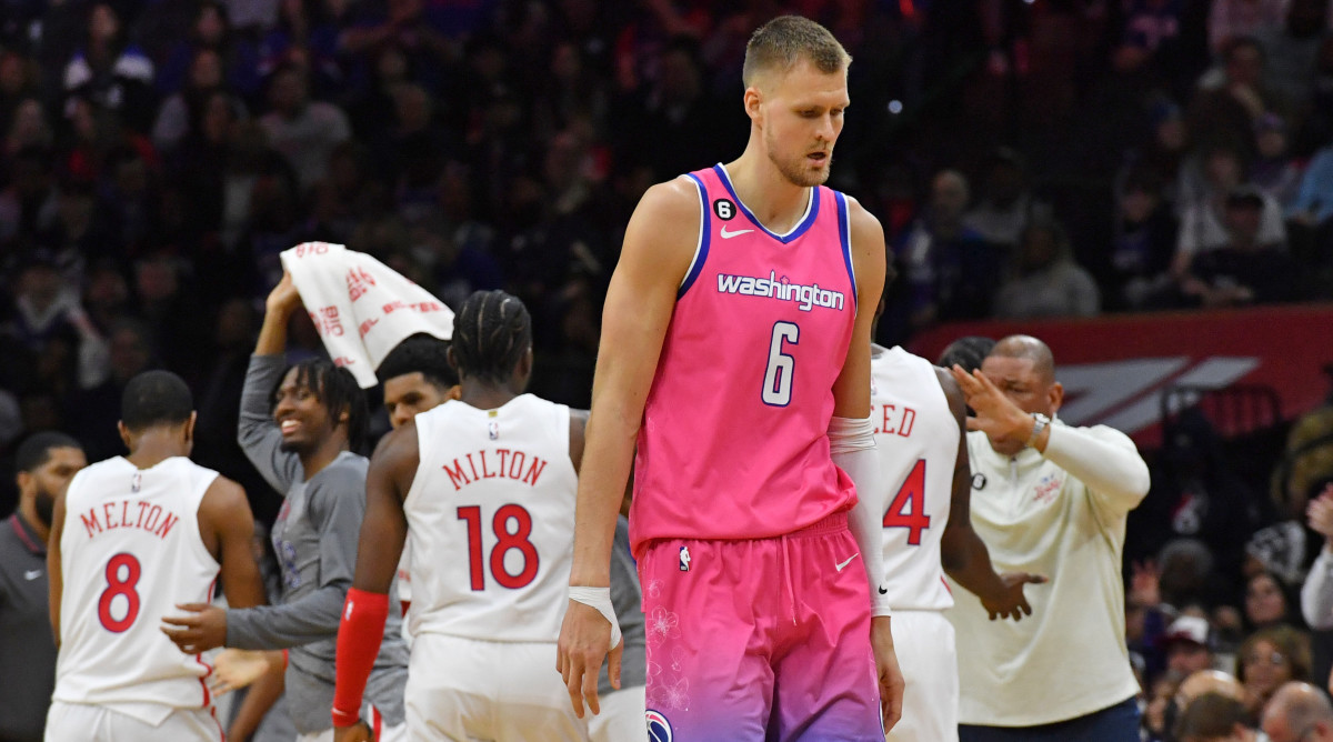 Wizards forward Kristaps Porzingis walks off the court as the 76ers celebrate behind him