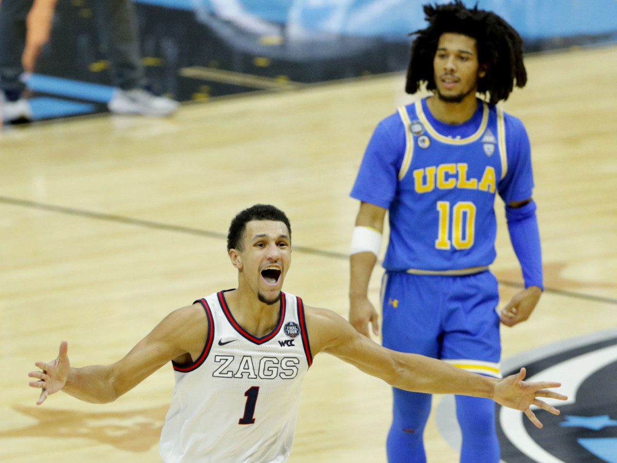 Gonzaga guard Jalen Suggs runs to the sidelines to celebrate after sinking a buzzer beater three-pointer to defeat UCLA in the 2021 NCAA tournament, with UCLA guard Tyger Campbell in the background in disbelief.