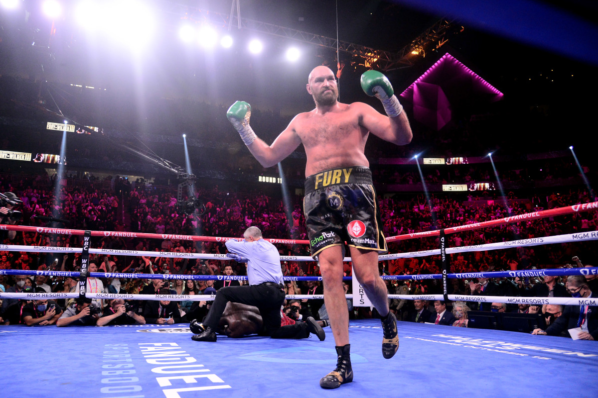 Tyson Fury stands with his fists raised while Deontay Wilder lays behind him knocked out