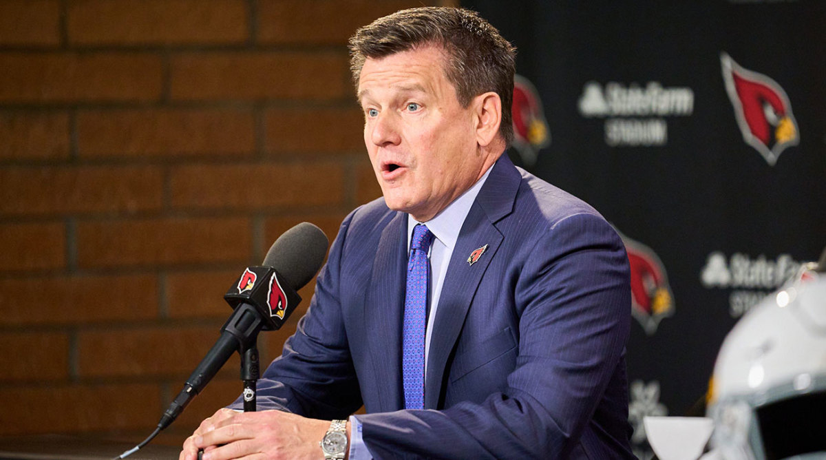 Michael Bidwill seated at a podium with a Cardinals microphone stand and backdrop