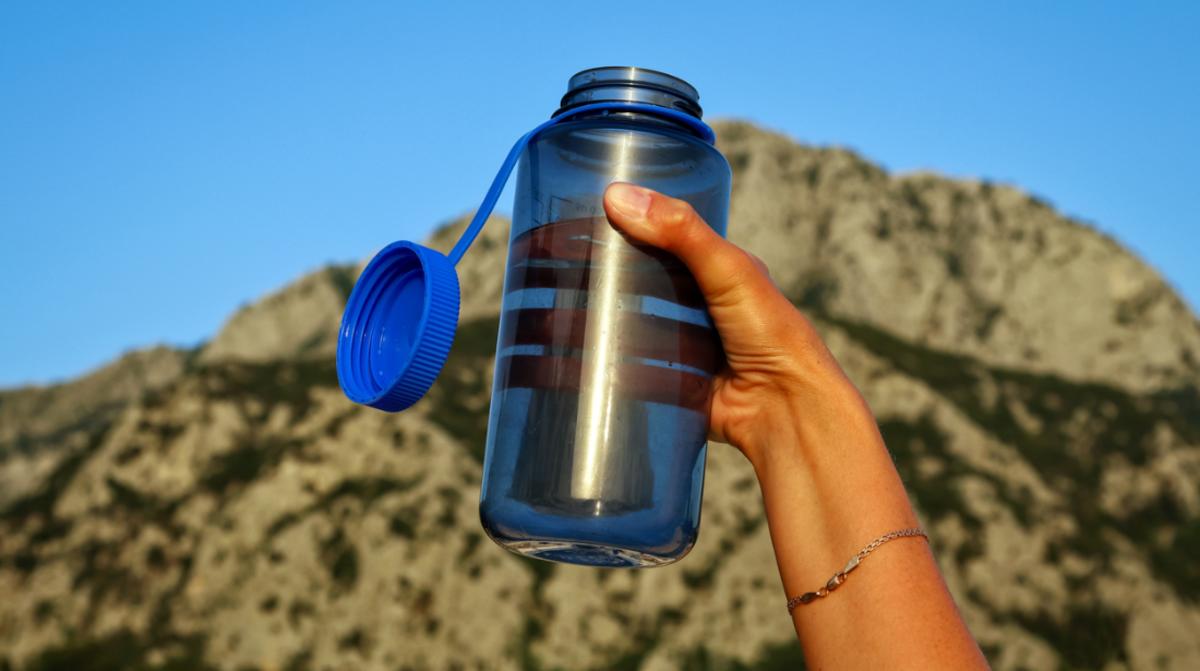 A person outside holding a transparent blue water bottle
