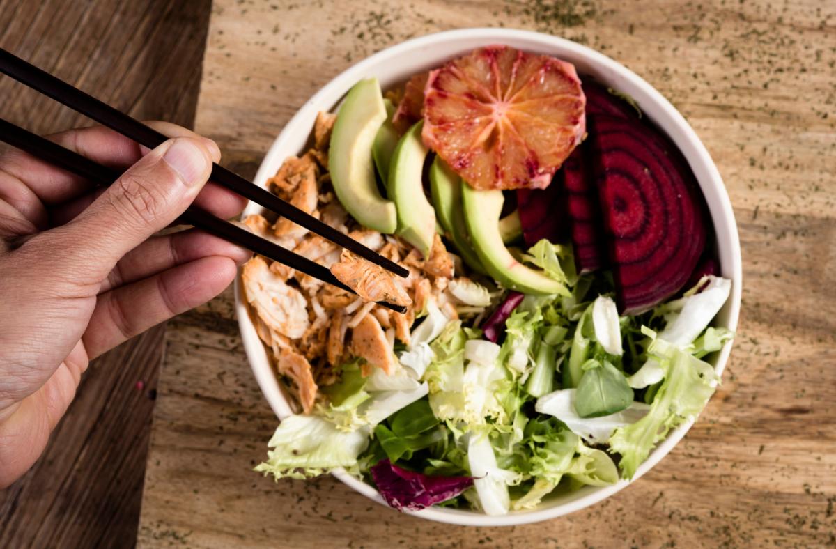 Person eating a chicken, avocado and beet salad with chopsticks