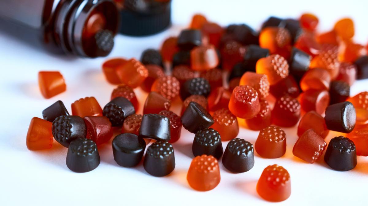 Berry-shaped gummy vitamins spilling out of a glass bottle