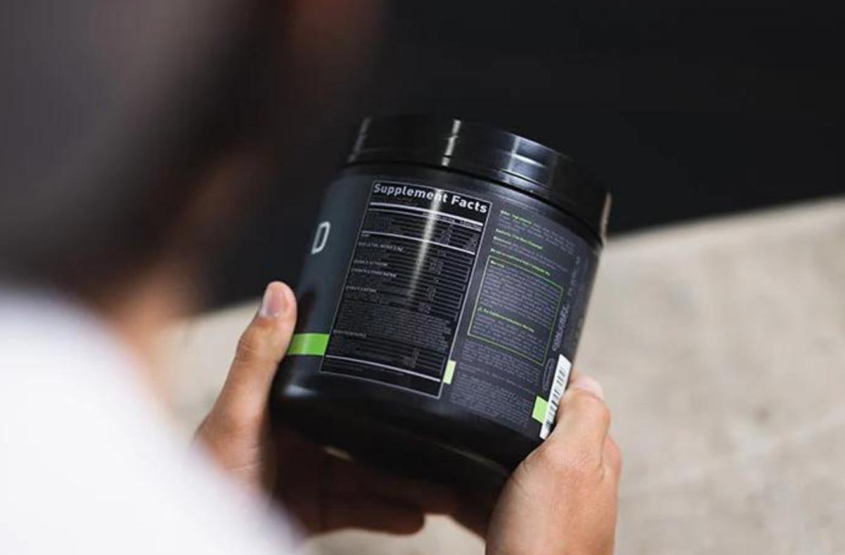 A person reading the supplement facts on a container of Kaged pre-workout