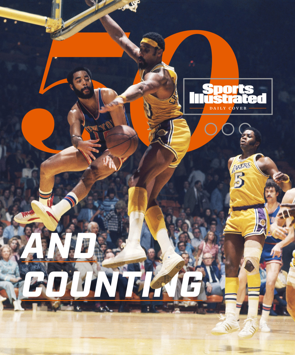 Clyde Frazier passes the ball around Wilt Chamberlain to set up a basket for the Knicks.