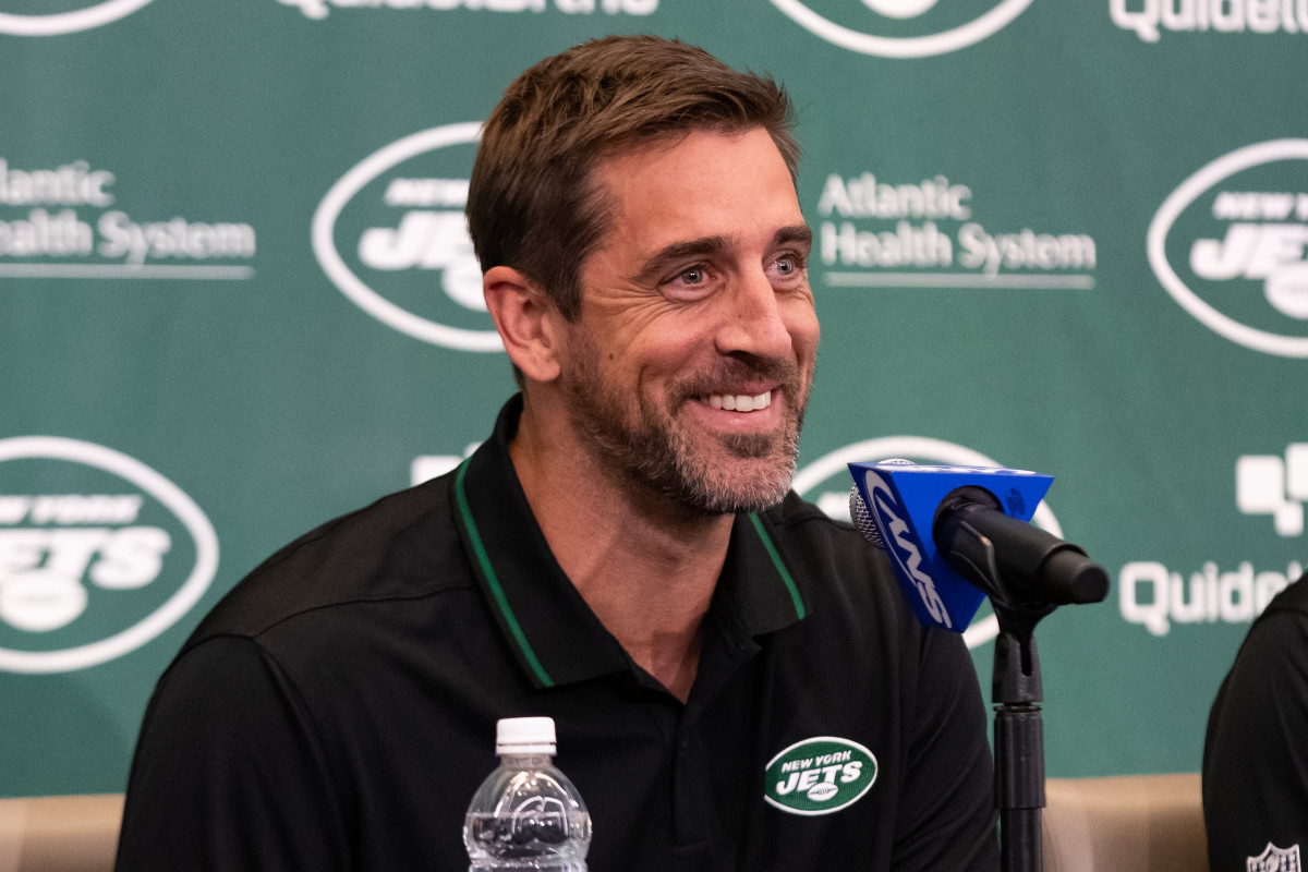 Aaron Rodgers talks into a microphone wearing a Jets shirt