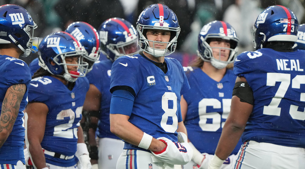 Daniel Jones looks to the sideline without much expression as teammates huddle around him.