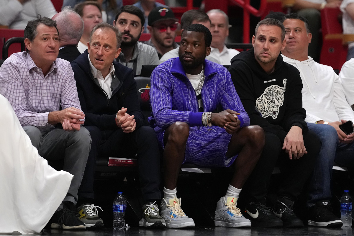 Men sit courtside at a basketball game, including Josh Harris, Meek Mill and Michael Rubin