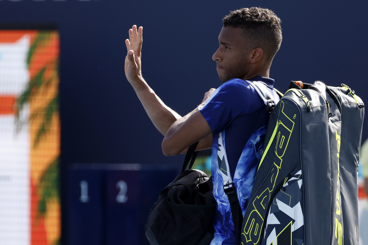 Felix Auger-Aliassime waves to the crowd holding a bag with his tennis rackets inside