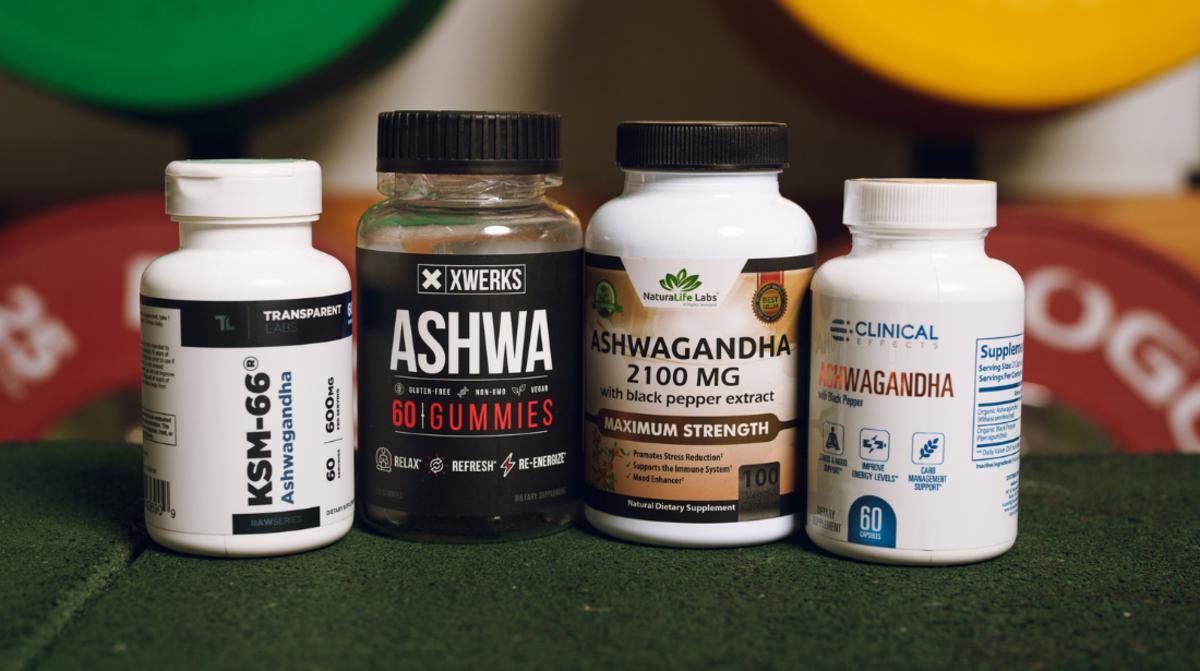 Four different bottles of Ashwagandha supplements are pictured in a row, flanked by workout equipment in the background