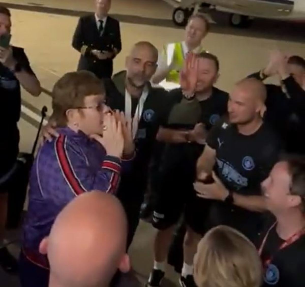 Man City manager Pep Guardiola pictured raising his hand to tell his players to be quiet as music legend Elton John delivers an impromptu team-talk on the tarmac of Manchester Airport in June 2023