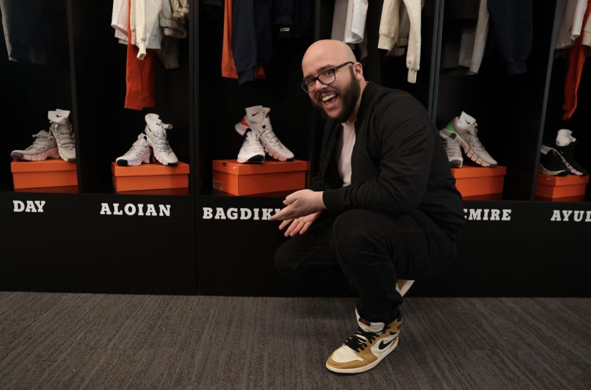 Social media producer Ryan Bagdikian kneels down in front of a locker with shoes and his name on it