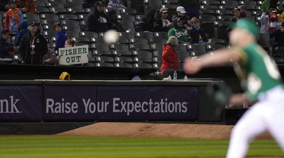 An Oakland Athletics fan holds up a “Fisher Out” sign directed at owner John Fisher as a reliever warms up in the foreground