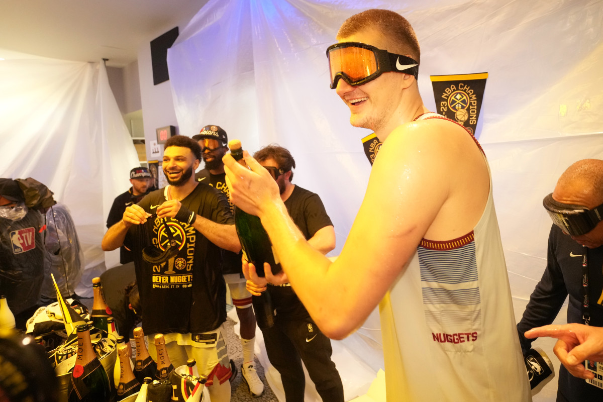 Nikola Jokić sprays champagne on his teammates after winning the NBA title.
