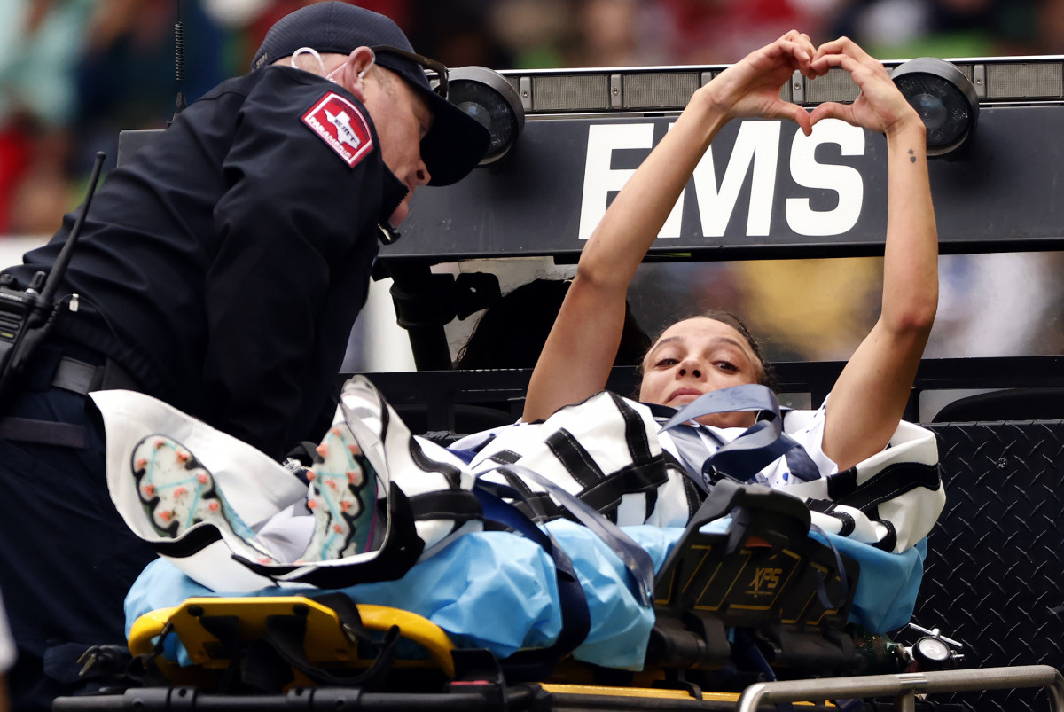 USWNT player Mallory Swanson holds her hands up in the shape of a heart as she is stretchered off the field.