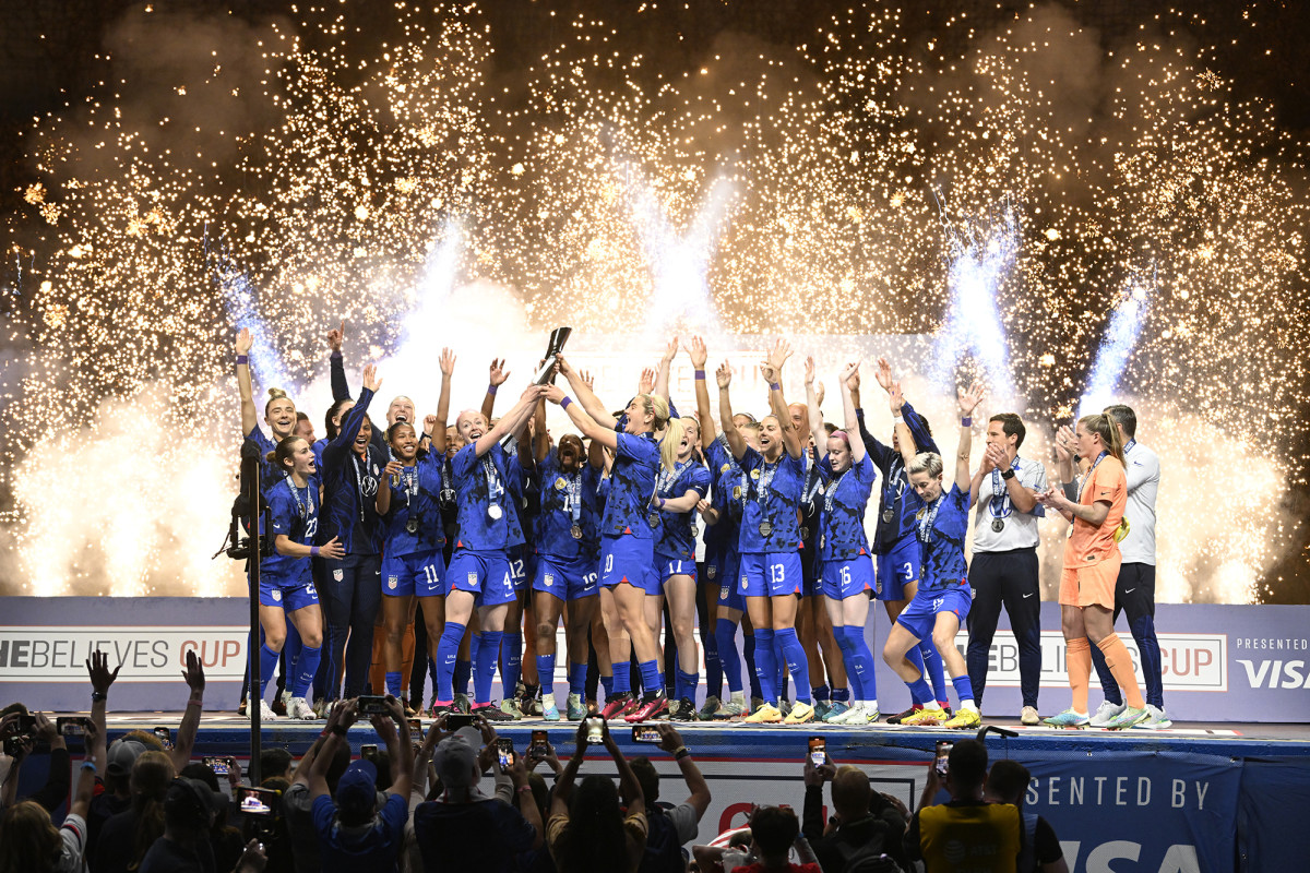 The USWNT celebrates winning the SheBelieves Cup with fireworks in the background.