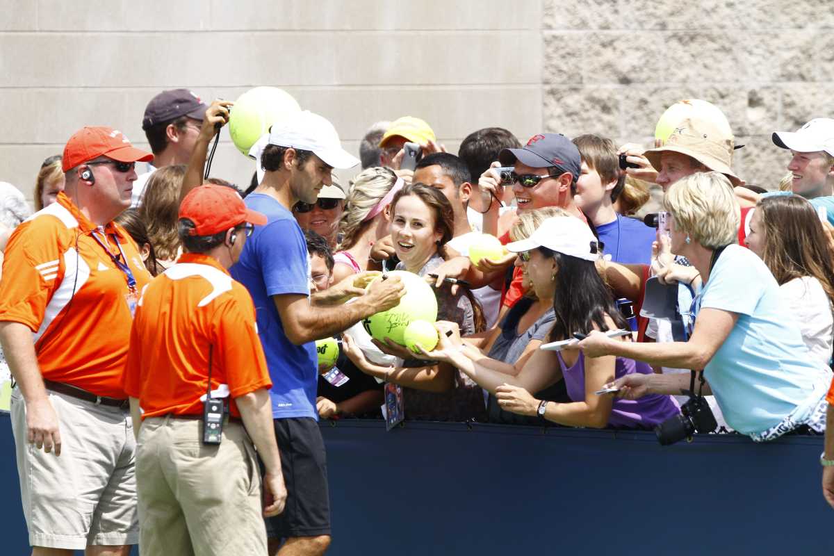 Roger Federer signs a giant tennis ball as fans gather at the barricade