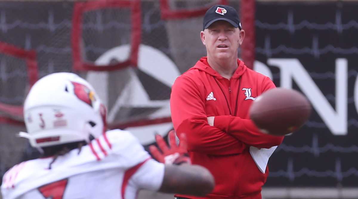 Louisville coach Jeff Brohm watches spring practice while a player catches a pass in the foreground