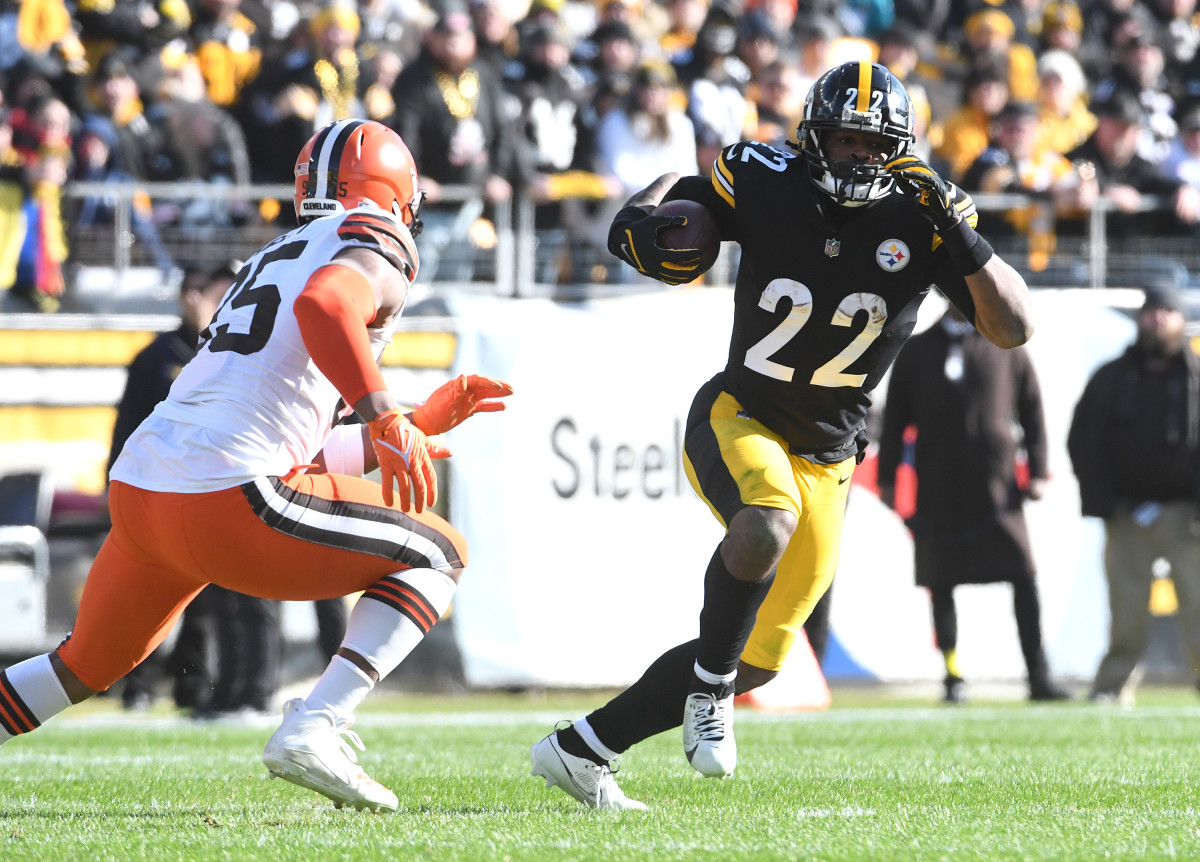 Najee Harris runs with the ball as a Browns defender runs toward him