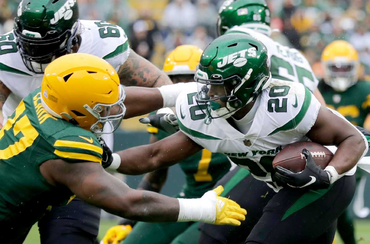 Kenny Clark reaches as Jets running back Breece Hall holds the ball and pushes him away with one arm