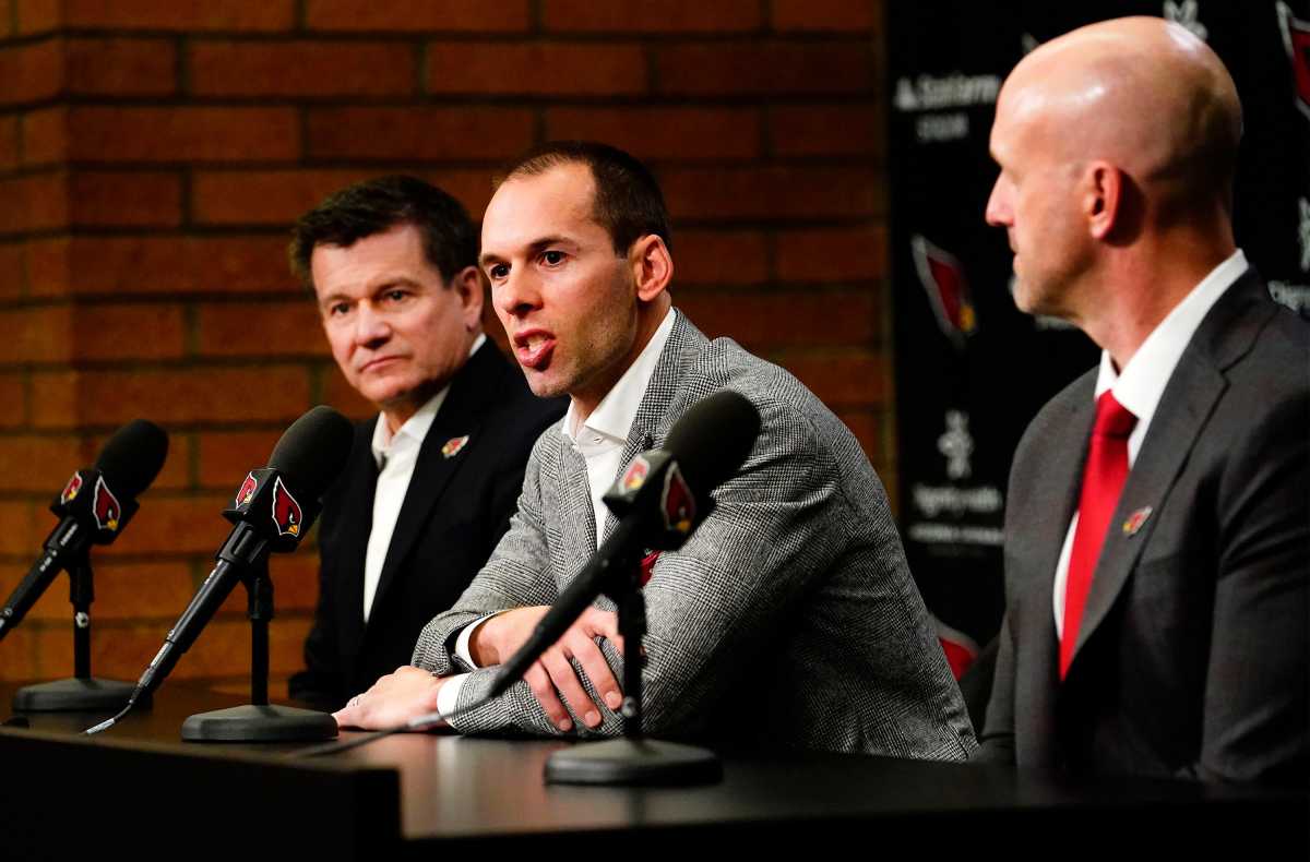 Jonathan gannon sits in front of a microphone wearing a suit