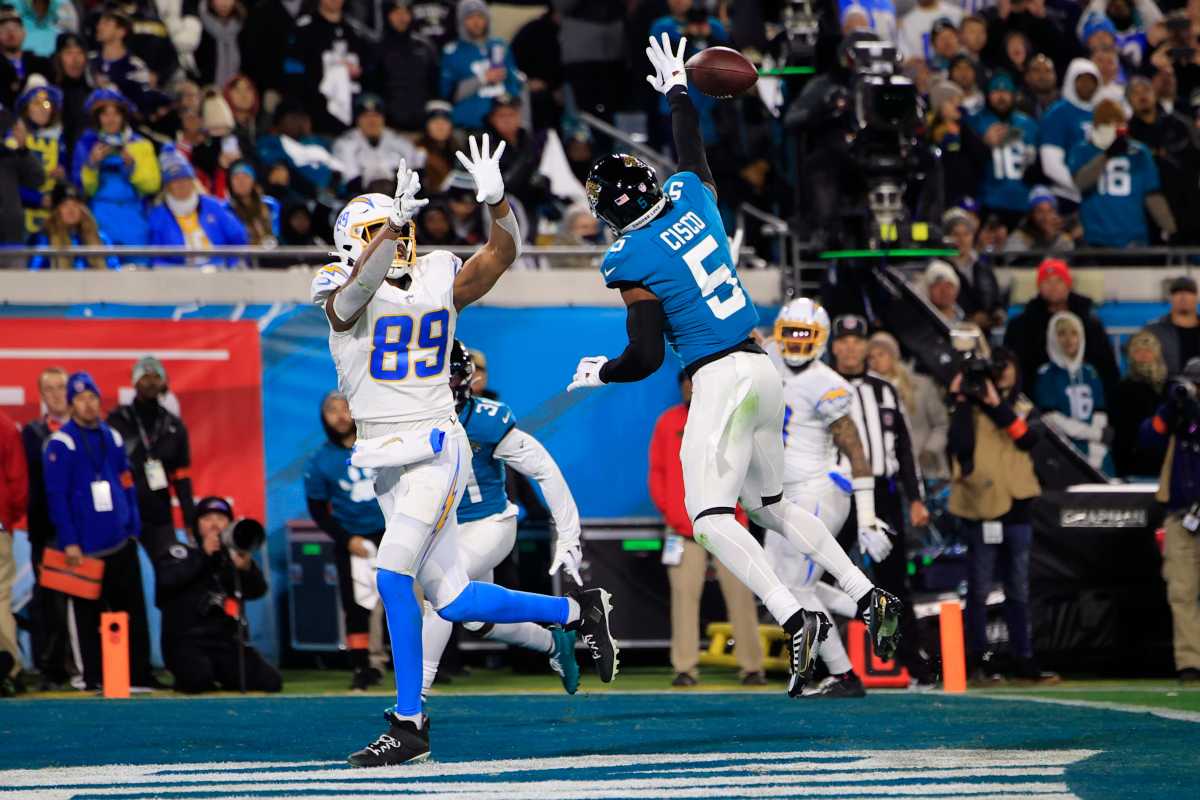 Andre Cisco jumps up with his hand straight up blocking the ball as a chargers player stands behind him trying to catch it