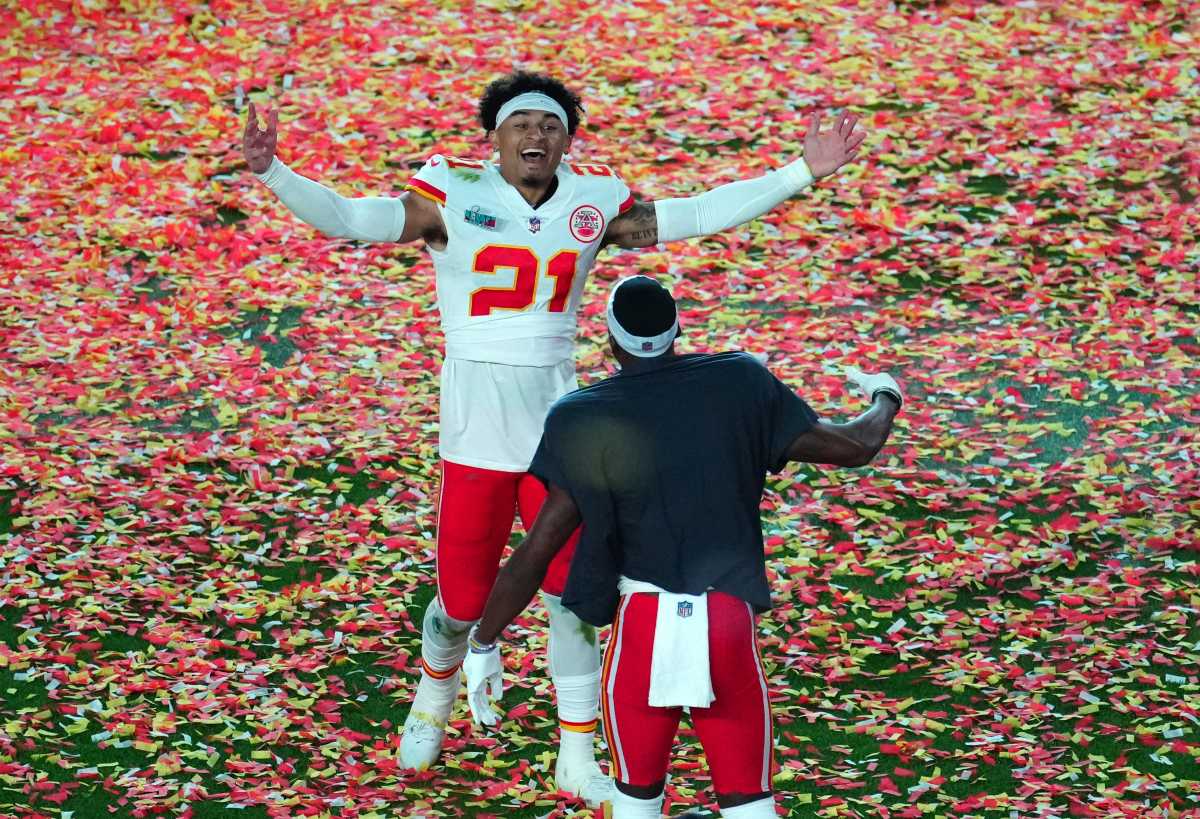 Trent McDuffie puts his hands up wide in celebration, getting ready to embrace another teammate on a confetti-covered field