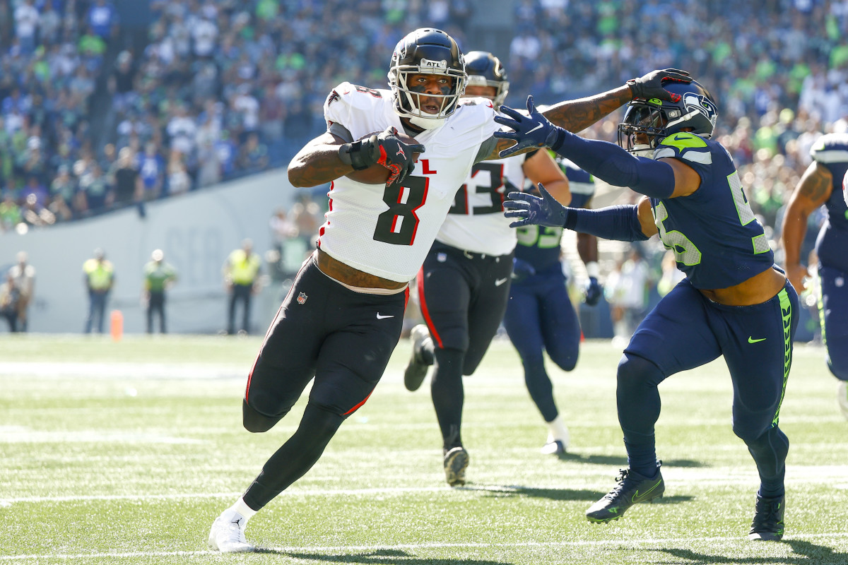 Kyle Pitts runs with the ball in one hand, using his other arm to try to push away a Seahawks defender who is reaching for him