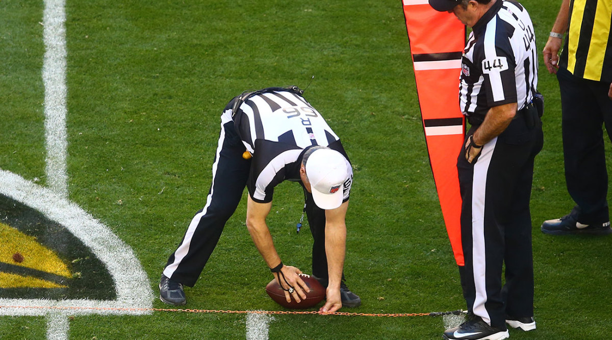 A ref leans down to place a football at an exact spot on a first-down chain