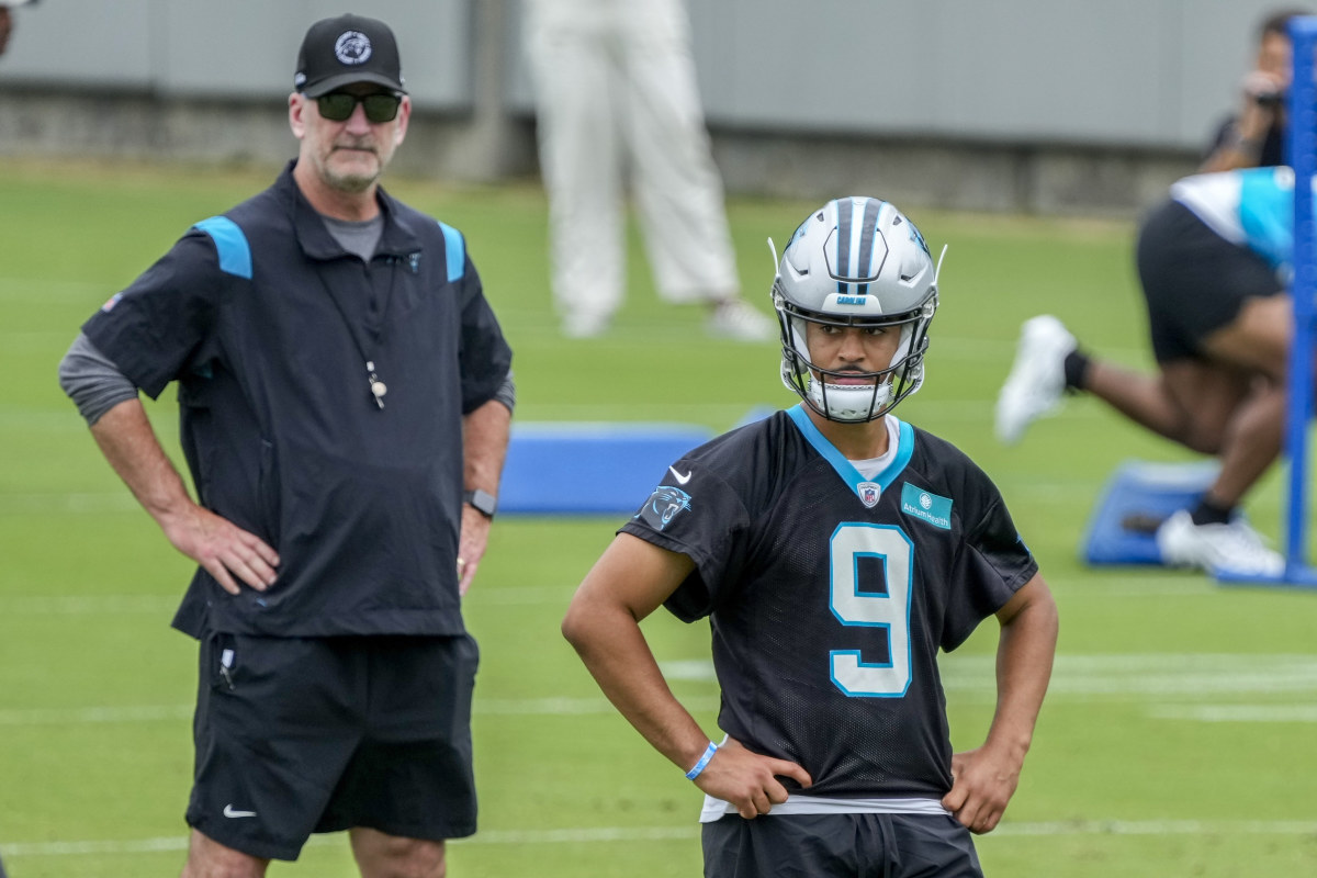 Frank Reich stands behind Bryce Young as they both watch something with their hands on their hips