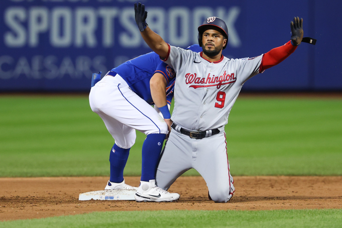 Jeimer Candelario kneels on the base and puts his hands up in the air as a Mets player leans down beside him