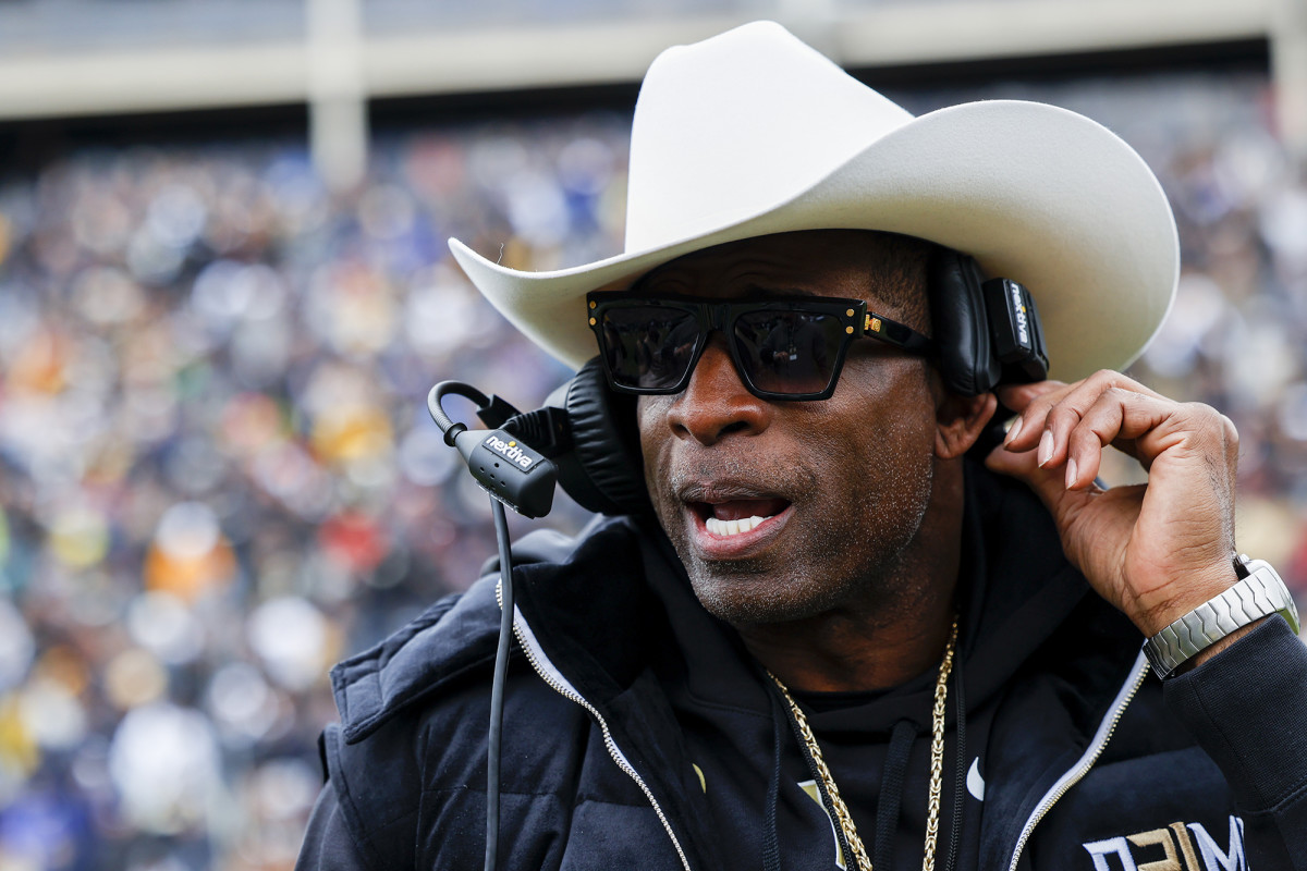 Colorado football coach Deion Sanders wears a cowboy hat on the sidelines while talking into his headset.