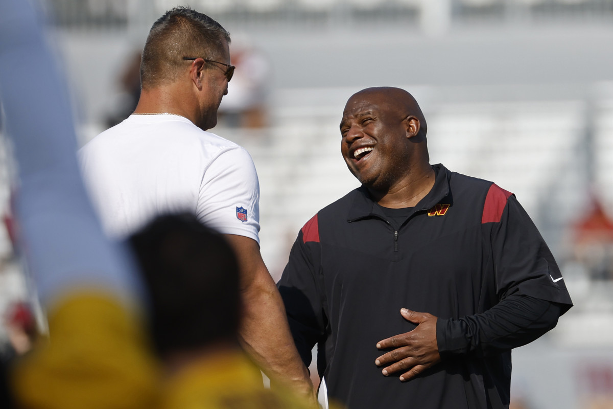 Washington Commanders assistant head coach/offensive coordinator Eric Bieniemy (R) jokes with Commanders defensive line coach Jeff Zgonina (L) during warmup on day three of Commanders training camp at OrthoVirginia Training Center