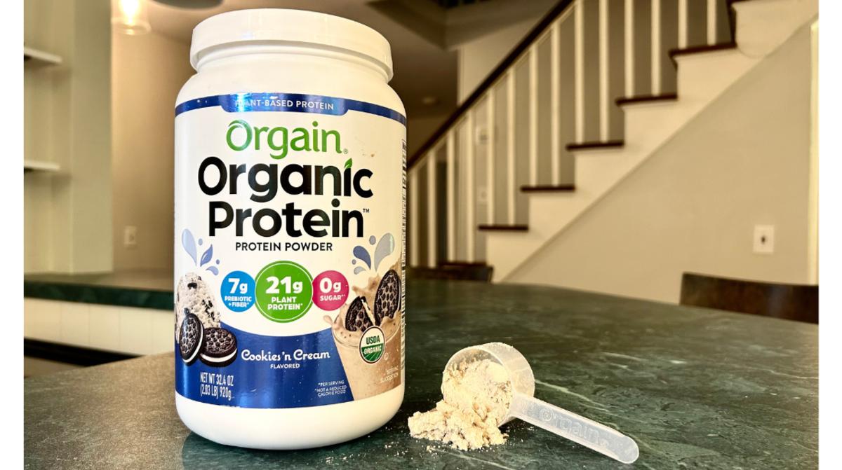 A tub of Orgain organic protein powder in Cookies 'n Cream flavor on a granite countertop