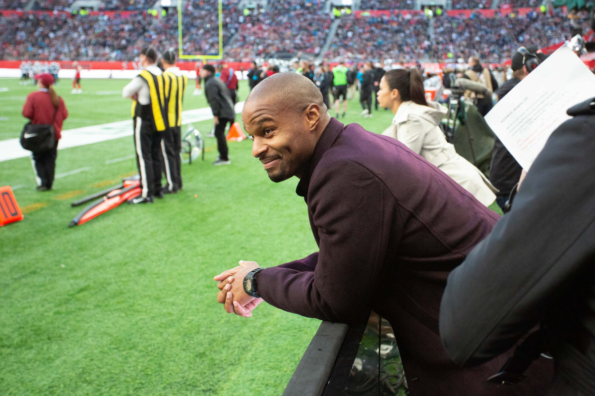 Osi Umenyiora smiles and leans in from the first row of the stands at a 2019 NFL game in London