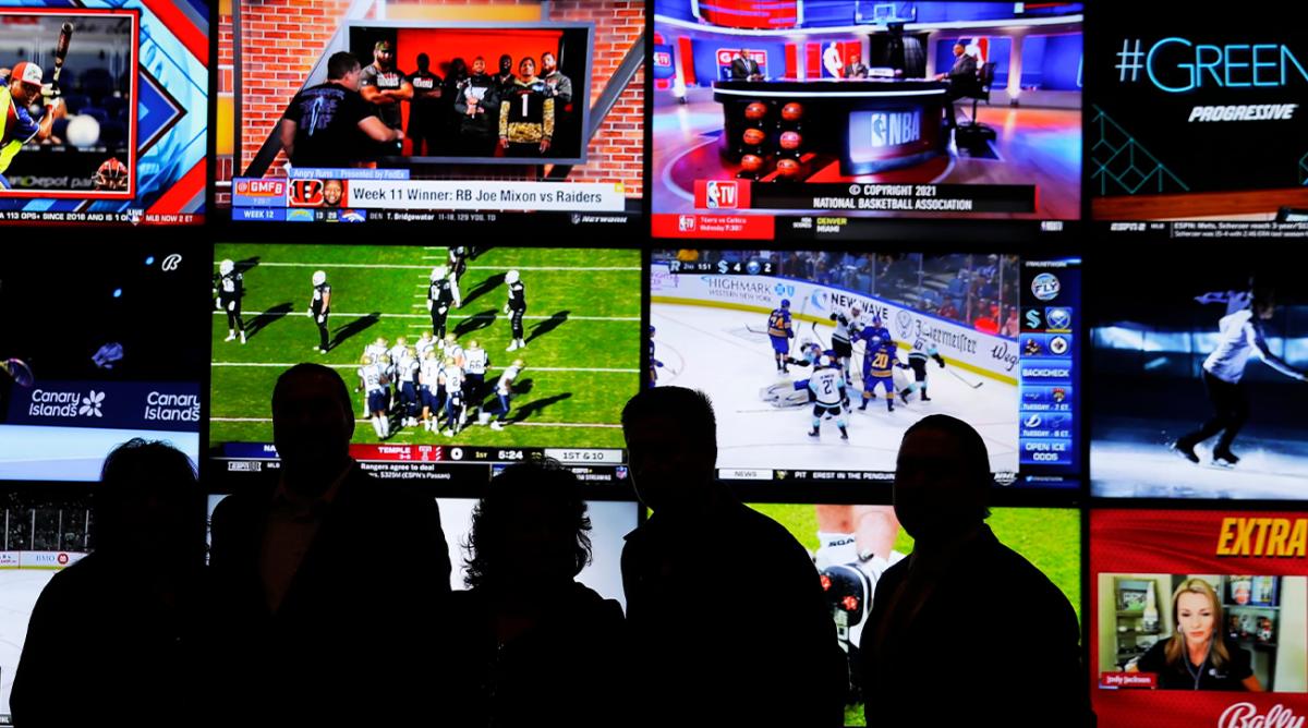 A group of people stand in front of a wall of televisions showing a variety of sports during the opening ceremony of the Oneida Casino’s sports betting operation on Nov. 30, 2021, in Ashwaubenon, Wis.