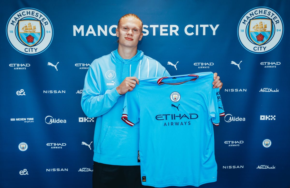 Erling Haaland pictured holding up a Manchester City jersey after signing for the club from Borussia Dortmund in 2022