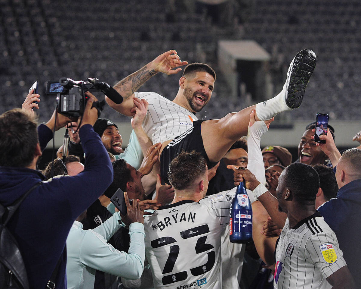 Aleksandar Mitrovic is held up by his Fulham teammates as they celebrate winning promotion to the Premier League in April 2022