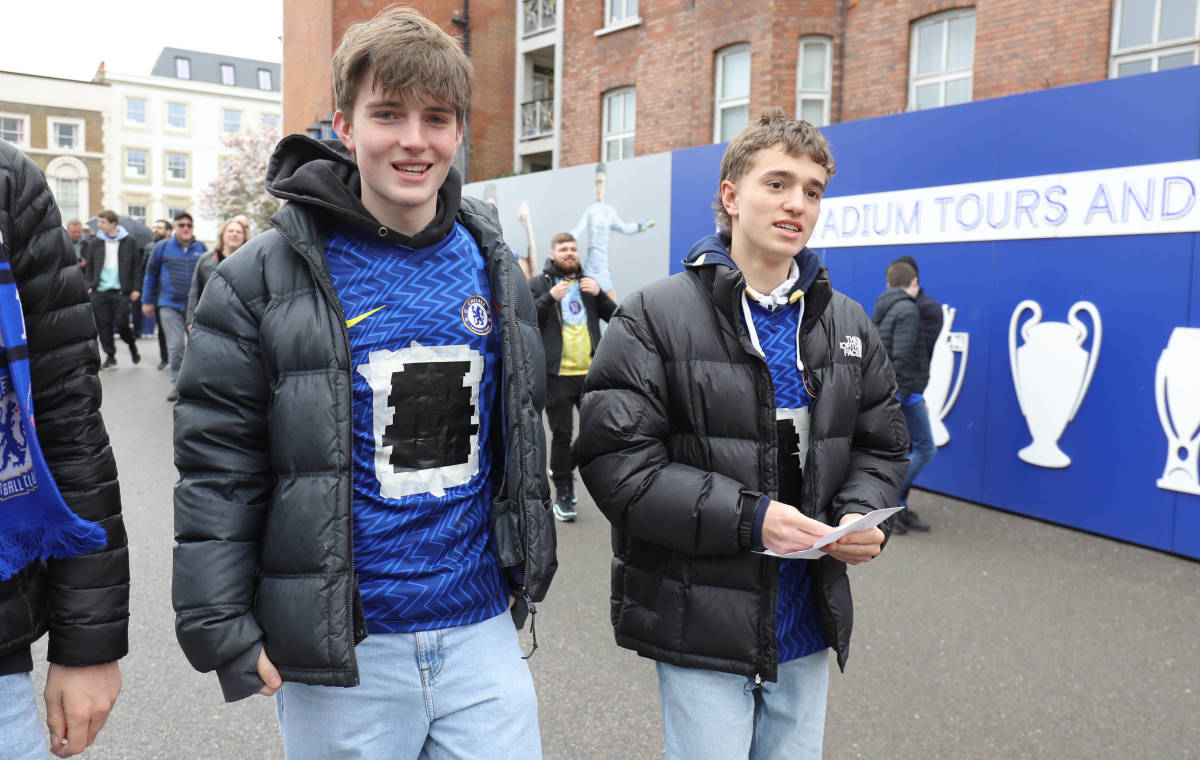 Two young Chelsea fans arrive at Stamford Bridge with tape covering the Three logo on their jerseys