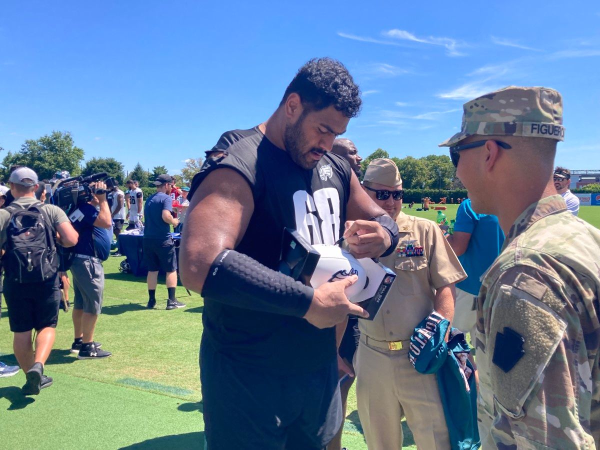 Jordan Mailata signs a football during Eagles' Military Day at camp