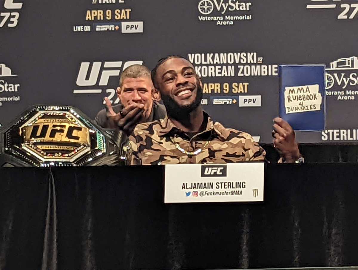 Bantamweight champion Aljamain Sterling holds an "MMA Rulebook 4 Dummies" to taunt interim champion Petr Yan (not pictured) during a press conference at UFC 273.