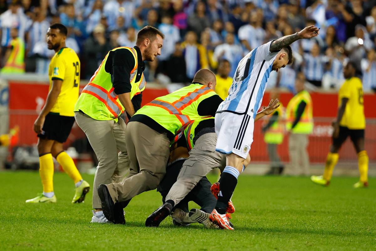 Lionel Messi pictured (right) struggling to stay on his feet as a pitch invader is tackled by security staff nearby during Argentina's game against Jamaica in September 2022