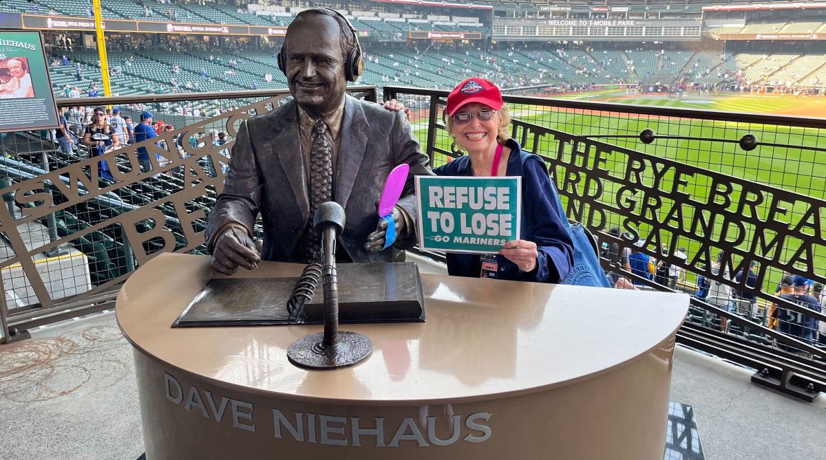 Marilyn Niehaus, the widow of former Mariners broadcaster Dave Niehaus, poses with a statue of him at T-Mobile Park.