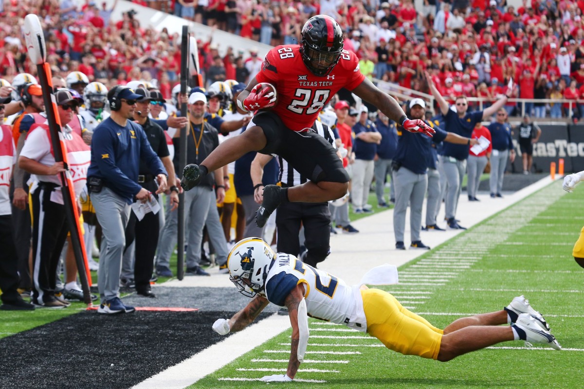 Oct 22, 2022; Lubbock, Texas, USA; Texas Tech Red Raiders running back Tahj Brooks (28) hurdles West Virginia Mountaineers defensive back Davis Mallinger (27) in the first half at Jones AT&T Stadium and Cody Campbell Field.